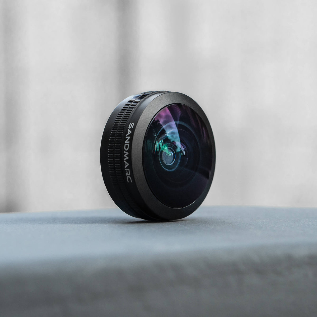 SANDMARC Fisheye Lens 10mm standing upright on a grey fabric surface against a soft white curtain background