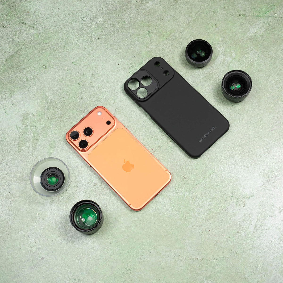 Overhead flat lay of iPhone and SANDMARC Standard Case — surrounded by SANDMARC fisheye, macro 25mm, telephoto 58mm, and wide lenses on a sage green textured surface