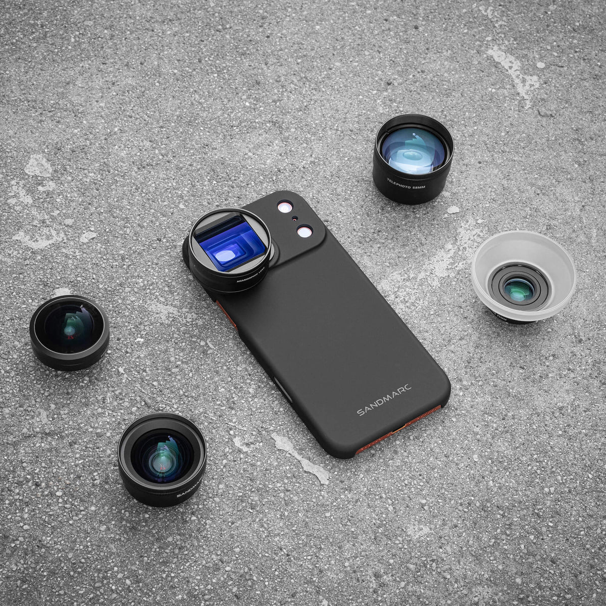 Overhead flat lay of the SANDMARC Pro Plus Edition on a concrete surface, showing a SANDMARC black Standard Case with Anamorphic Lens attached, surrounded by four lenses — Fisheye, Wide Angle, Telephoto 58mm, and Macro — laid out around the phone