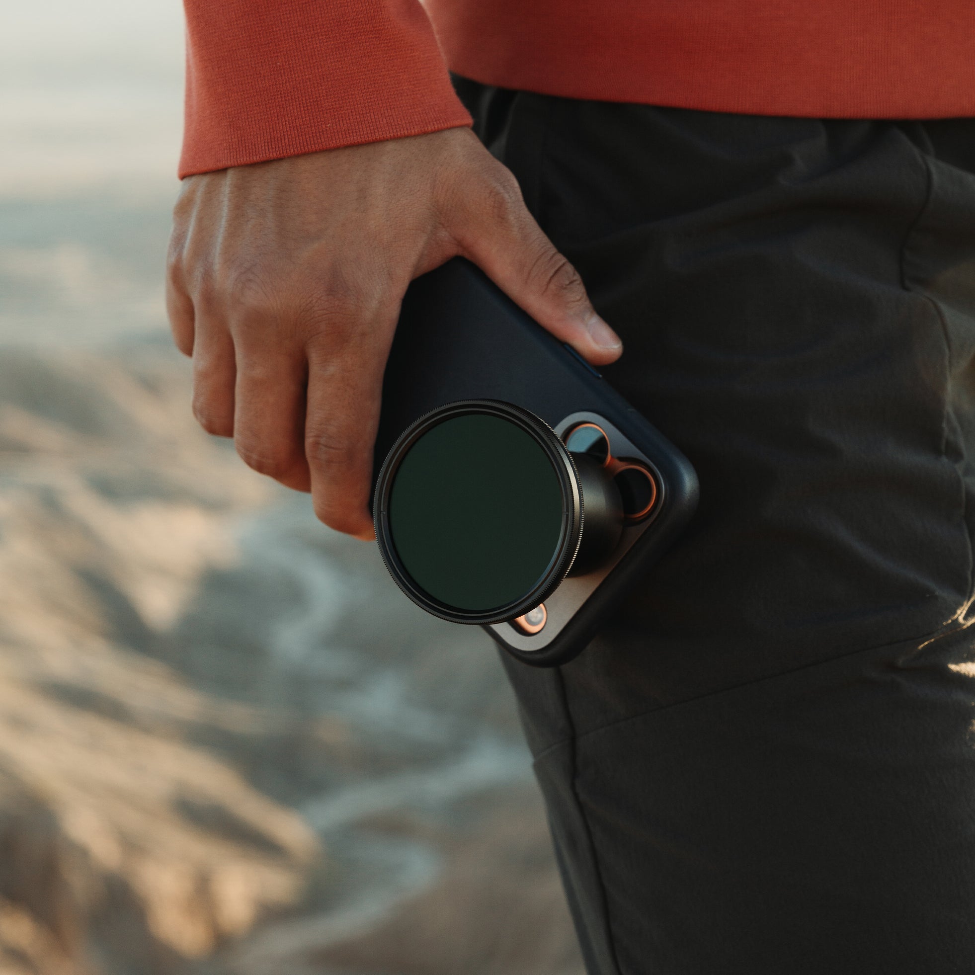 Person holding an iPhone with 48mm Lens and filter attachment against a blurred natural background.