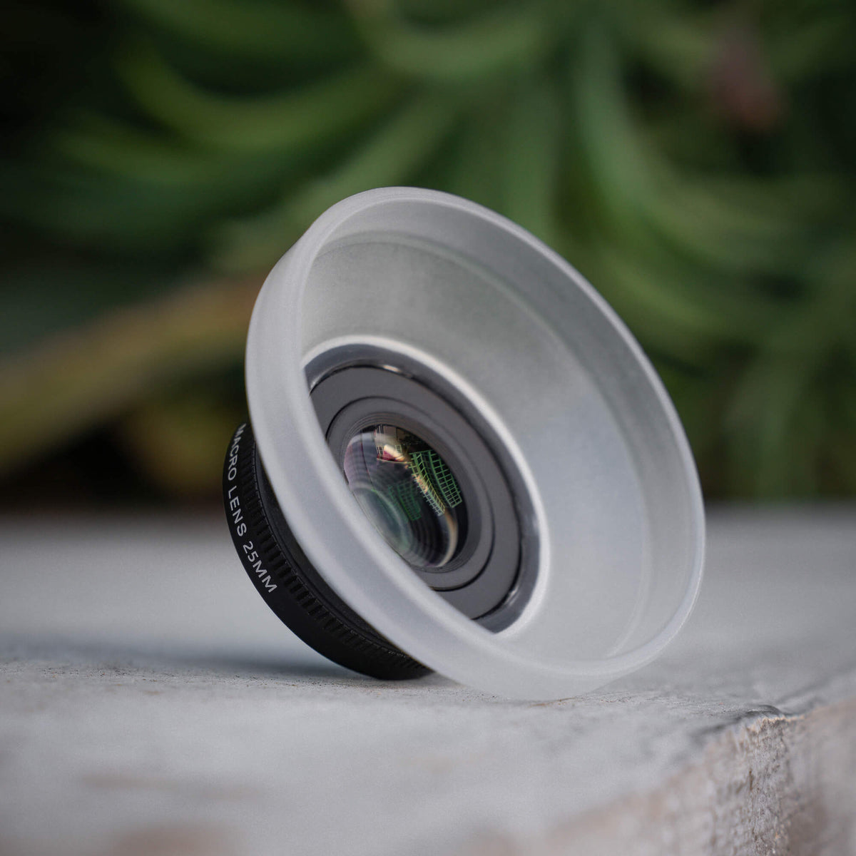 SANDMARC Macro Lens 25mm standing upright on a grey concrete surface with its translucent diffuser hood attached #type_macro 25mm