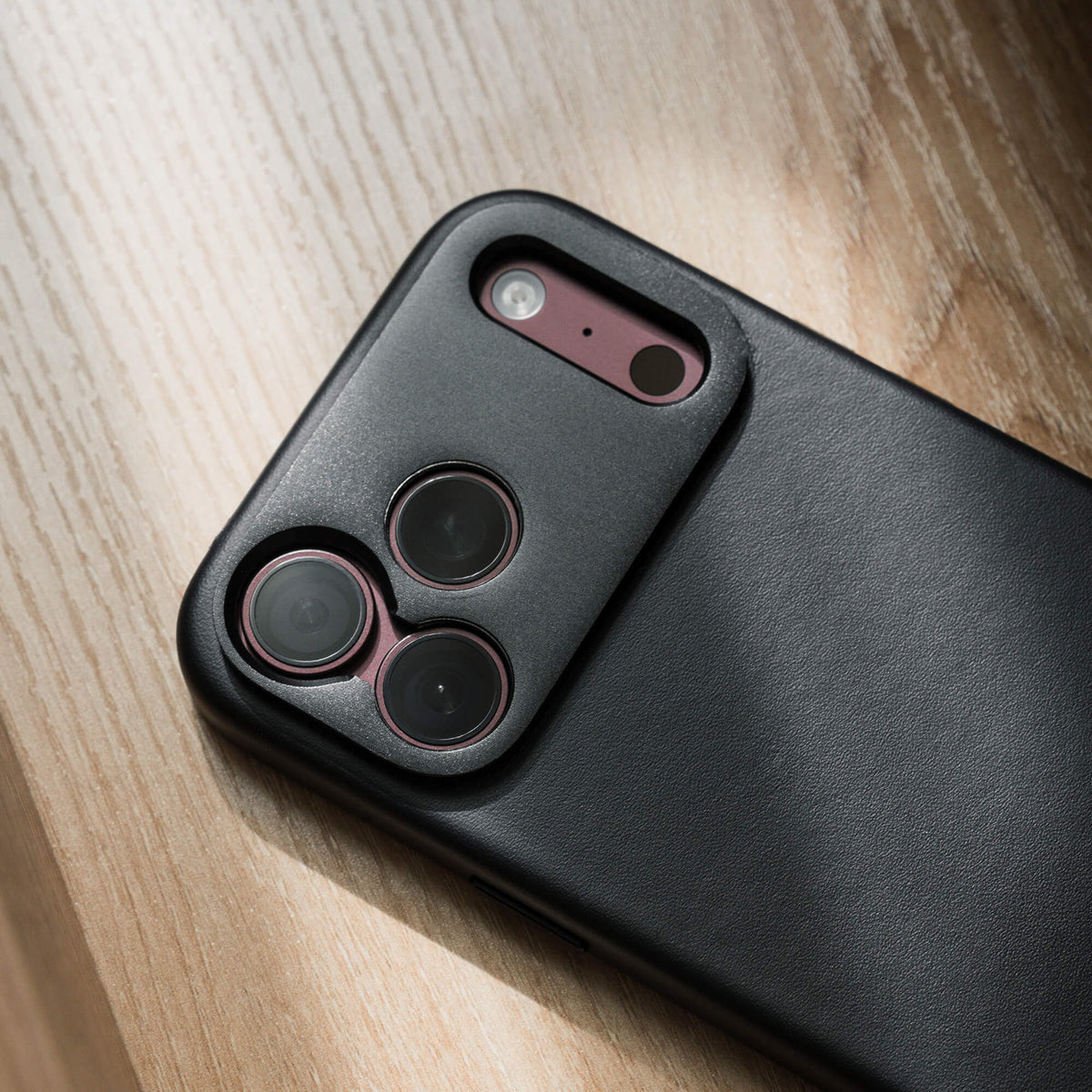 SANDMARC Pro Leather Case for iPhone 18 Pro in Black, close-up of camera cutout on a wooden surface.