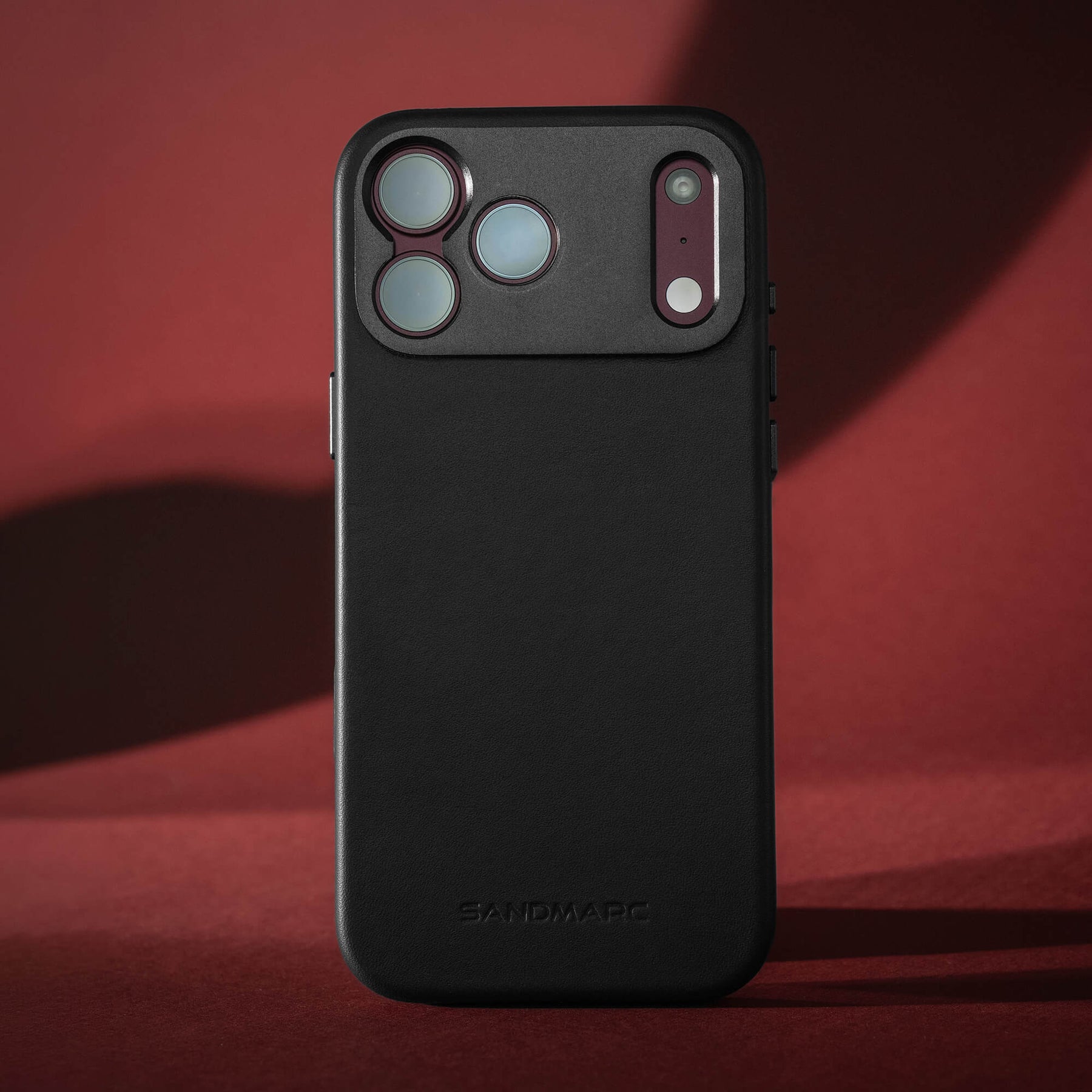 SANDMARC Pro Leather Case for iPhone 18 Pro in Black, standing upright on a dark red background.