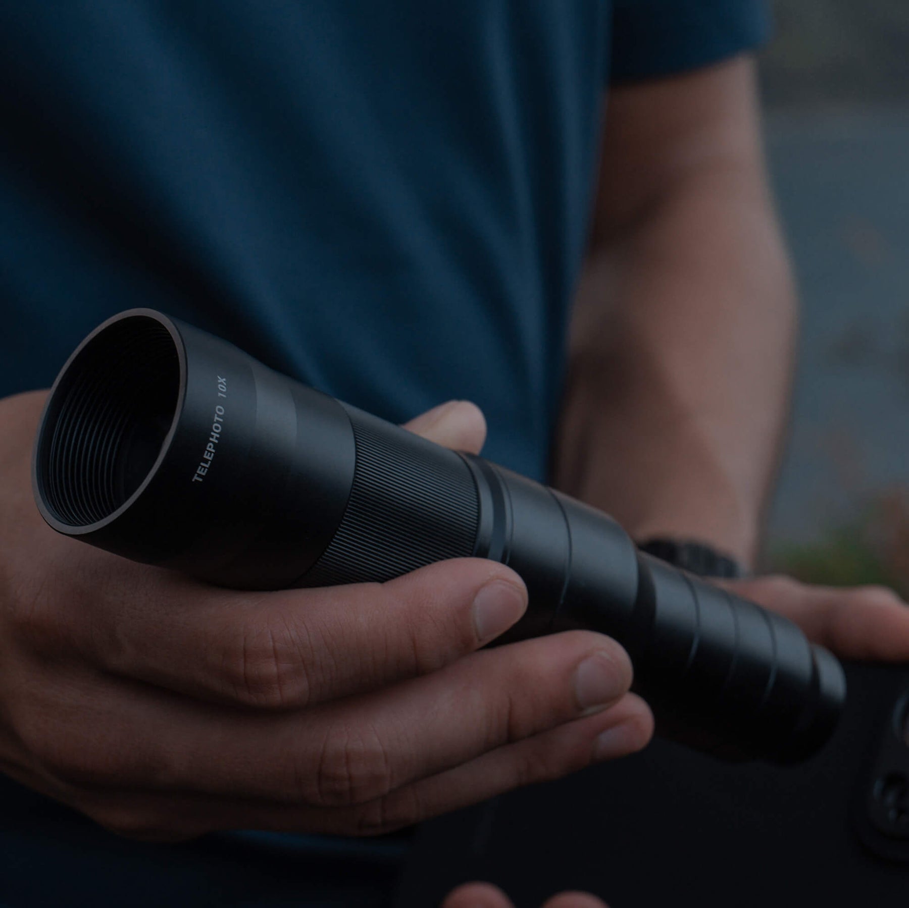 SANDMARC Telephoto 10x Lens held in a hand with a person wearing a blue shirt in the blurred background