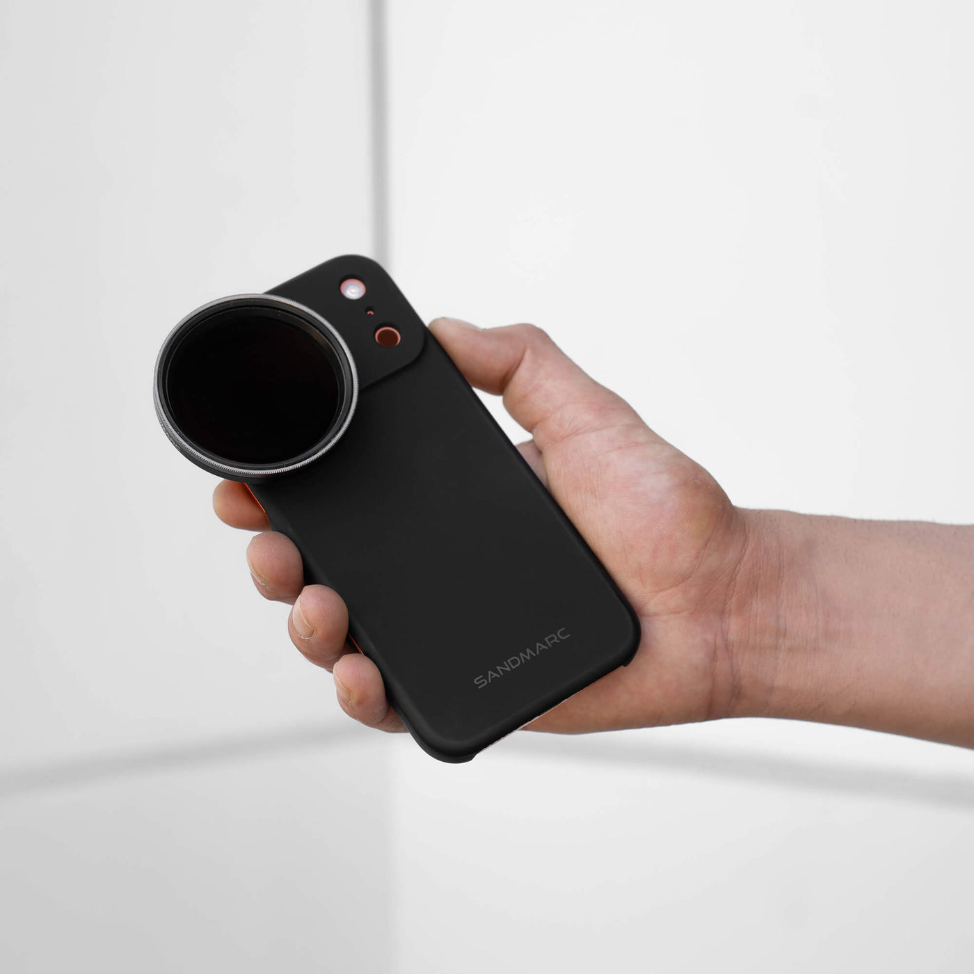 Hand holding a iPhone with a SANDMARCED black case and a Variable ND filter mounted, on a light gray background.