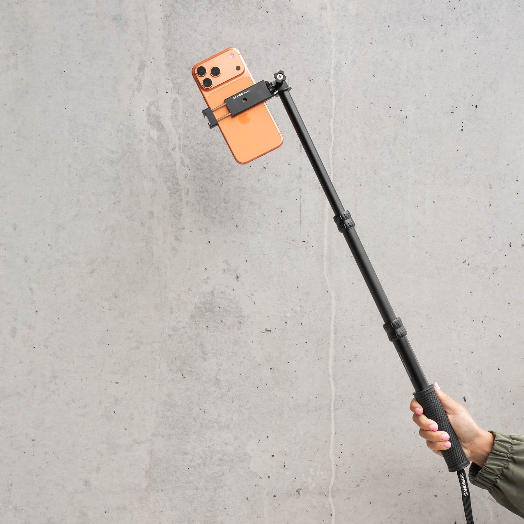 Photgrapher holding SANDMARC Pole with iPhone 17 Pro Max attached on stone background
