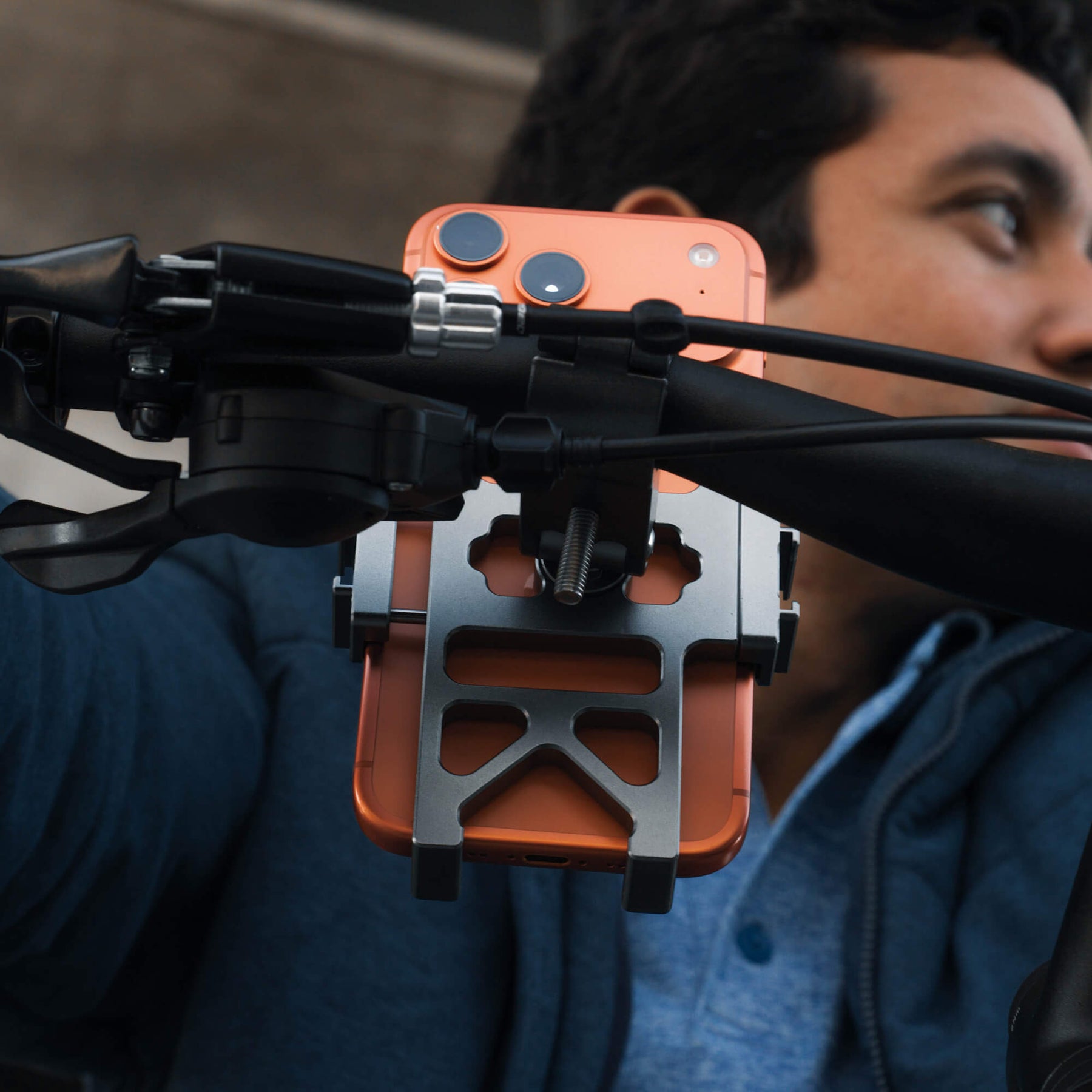 An orange iPhone securely attached to a bicycle handlebar using the SANDMARC Creator Bike Mount