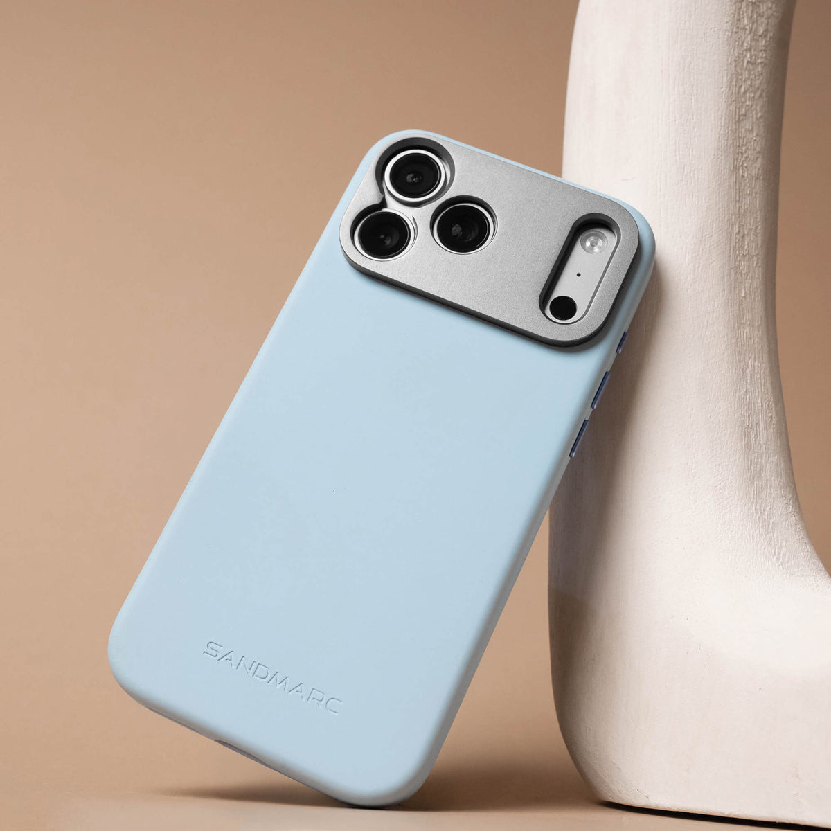 SANDMARC Pro Case for iPhone 18 Pro Max in Glacier blue, leaning against a white sculpted vase with a tan background