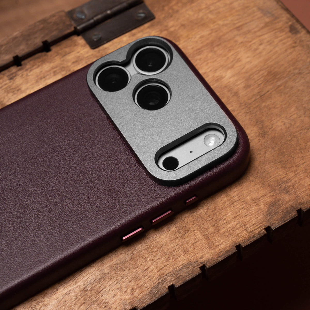 SANDMARC Pro Leather Case for iPhone 18 Pro in Burgundy, close-up of camera cutout on a wooden crate with a metal hinge