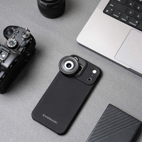 iPhone 18 Pro Max in a SANDMARC Black Standard Case with the Microscope Lens attached lying flat on a textured rust and grey concrete surface, showing the SANDMARC logo and circular lens element