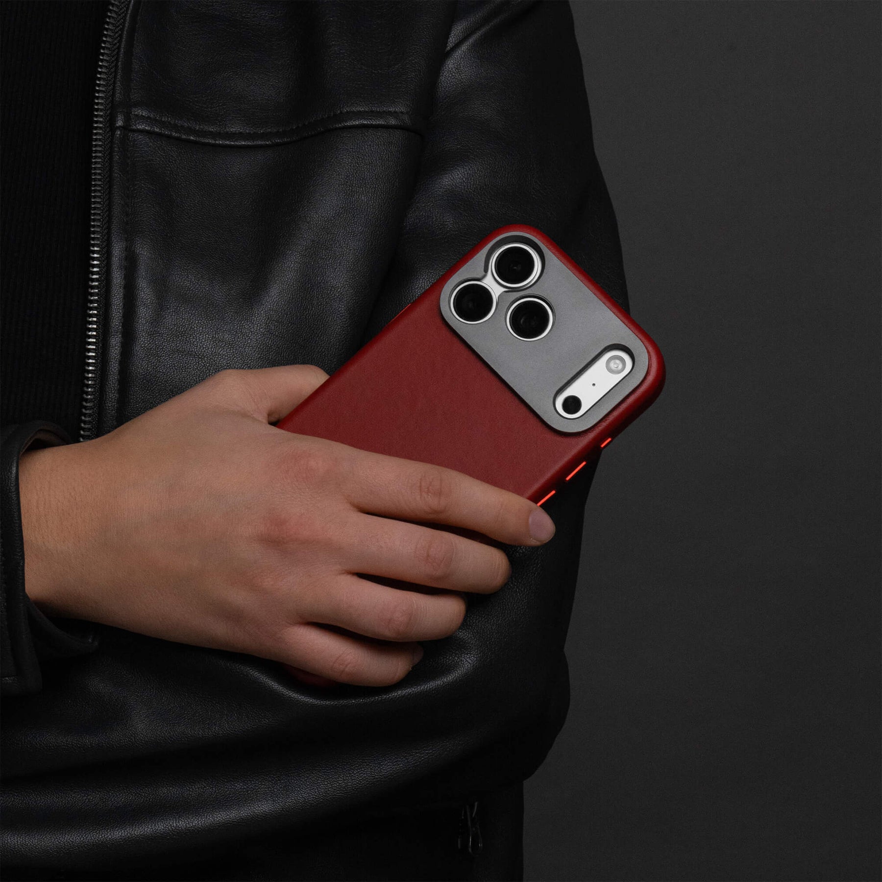 Woman holding an iPhone in the SANDMARC Pro Leather Case in red against their black leather jacket, showing the full-grain leather texture and aluminum camera mount