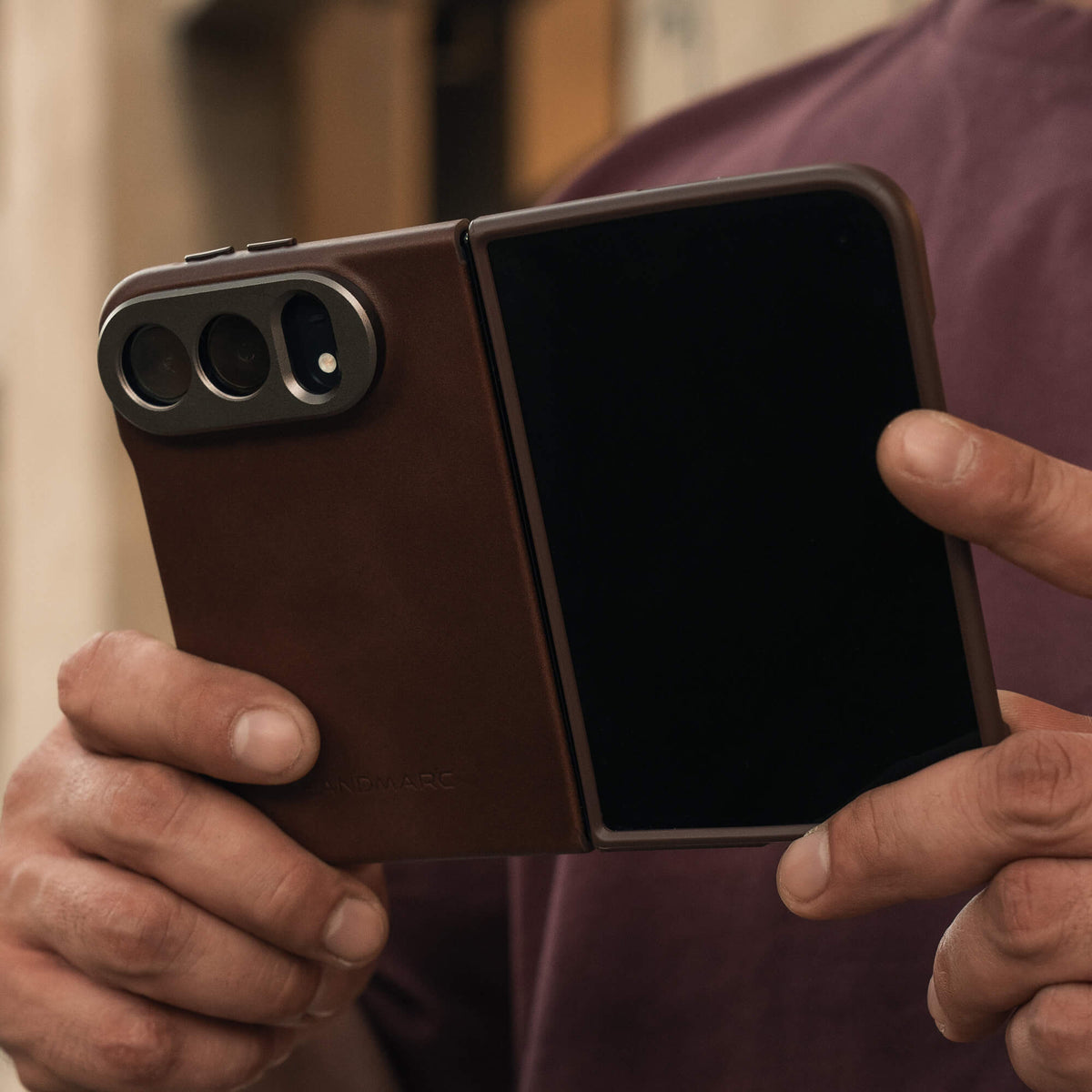 SANDMARC Pro Leather Case for iPhone Duo in Brown, held open to show the folding design, with a person behind